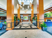 Spacious hotel lobby with tall wooden columns, modern light fixtures, potted plants, tiled floors, and contemporary seating areas.