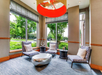 Modern lounge area with patterned chairs, a metallic coffee table, side tables, and large windows overlooking greenery.