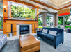 A modern hotel lobby features a dark blue sofa, leather ottoman, patterned armchair, fireplace, and large windows with garden views.