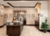 An open breakfast bar area with several countertops full of food including an island, art on the walls, and a tall potted plant.