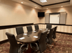 A meeting room with ornate carpet, an oval table lined with chairs in front of a white board and TV mounted on the wall.