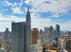 A cityscape view featuring the Empire State Building and surrounding skyscrapers under a partly cloudy sky.