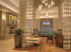 Hotel lobby with a cozy seating area, stone fireplace on the left, a teal sofa, a table with refreshments, and modern pendant lights above.