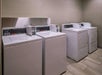 A laundry room with two white washing machines and two white dryers lined up against a beige wall.