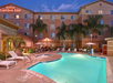 Outdoor hotel pool area at night with lounge chairs and umbrellas surrounded by a building with the Hilton Garden Inn sign.