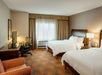 Two queen beds, bedside lamps, air condition, seating area, desk, and TV in a guest room.