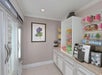 Small convenience store corner with beverages in coolers, a snack shelf, wine bottles, a coffee machine, and various packaged goods. Wall art displays a flower painting.