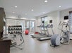 A gym with treadmills, an elliptical, stationary bike, weight rack, and an exercise ball. Large mirrors and windows line the walls.