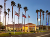 Hotel entrance with a tile roof, surrounded by tall palm trees and three flagpoles displaying the U.S., California, and hotel flags.