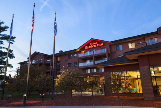 Exterior view of a Hilton Garden Inn hotel with flags and evening sky in the background.