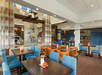 Hotel dining area with wooden tables, blue and brown chairs, modern lighting, and a decorative wall art display.