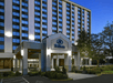 Exterior view of a multi-story hotel building with the Hilton logo, featuring large windows and an entrance with landscaping.