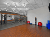 A gym with exercise equipment, including two stability balls, weights on a rack, a row of stationary bikes, and fitness mats on hardwood flooring.