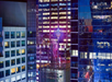 A brightly lit New Year's Eve ball is positioned atop a building in a cityscape at night, surrounded by tall, illuminated skyscrapers.