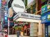 Hilton Times Square entrance with signage, surrounded by neighboring businesses including Applebee's and ice cream shops.
