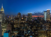 A nighttime cityscape with illuminated skyscrapers under a dark blue sky and an orange sunset on the horizon.