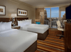 Two double beds, flat-screen TV, work desk, and a private balcony inside a guest room.