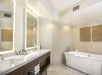 A lighted mirror, white sink, bath tub and shower inside an elegant guest bathroom.