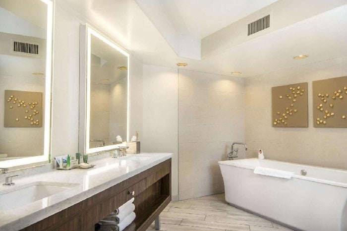 A lighted mirror, white sink, bath tub and shower inside an elegant guest bathroom.