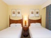 Two Queen beds and a lamp in between inside a guest room.
