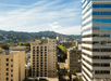 Wide shot of the city of Portland with trees in the distance and a blue cloudy sky overhead on a bright sunny day.