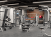 A large fitness center with gray flooring, several pieces of weight equipment, and florescent lights overhead at the Hilton Portland Downtown.
