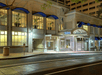 Street view of the beige stone exterior and front entrance to the Hilton Portland Downtown with blue awnings over the windows at night.