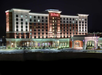 Illuminated multi-story Hilton hotel with a red sign, viewed at night. The building features a modern design with large windows and is surrounded by a parking lot.