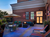 Outdoor seating area with tables, chairs, a fire pit, and an umbrella. Brick building with "Aura Spa & Salon" sign. Evening lighting creates a cozy atmosphere.