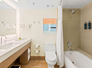 Modern bathroom with a large mirror, sink, toilet, bathtub with shower, and beige tiles. Wall art and neatly arranged towels are present.