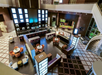 A spacious hotel lobby with modern decor, featuring a central bar area with seating, tables, and a nearby staircase leading to an upper level.