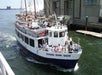 A white passenger boat named "Edward Rowe Snow" carrying people is moving away from a dock in a harbor, with buildings and another docked boat in the background.