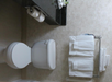 Bathroom with a toilet, two rolls of toilet paper, and a rack with neatly folded white towels.