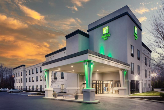 A Holiday Inn hotel building at sunset with a well-lit entrance and green accent lighting.