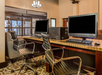 A small hotel business center with two computers on a wooden desk, two office chairs, and patterned carpet flooring.