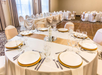 A round table set for a formal event with white plates, gold chargers, cutlery, glassware, and a central floral arrangement in an elegantly decorated banquet room.