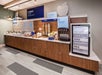 Hotel breakfast buffet area with cereal dispensers, a juice machine, and a refrigerator labeled for yogurt, eggs, and milk.