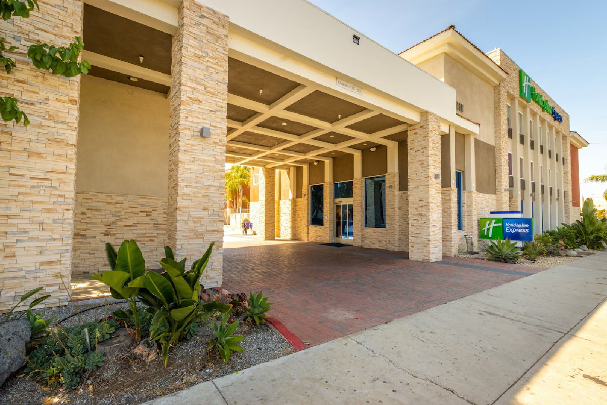 Entrance of a Holiday Inn Express hotel with stone facade, plants, and a sign on the right side.