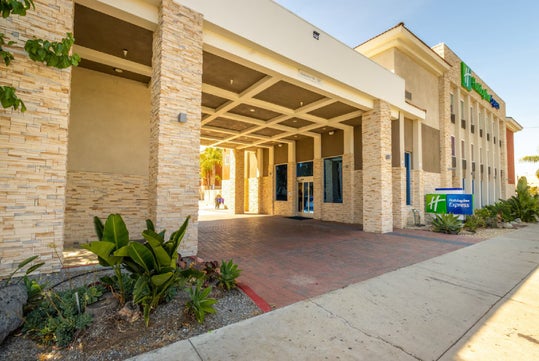 Entrance of a Holiday Inn Express hotel with stone facade, plants, and a sign on the right side.