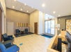Lobby area with blue chairs, striped wall art, and large glass doors. Social distancing markers are on the floor.