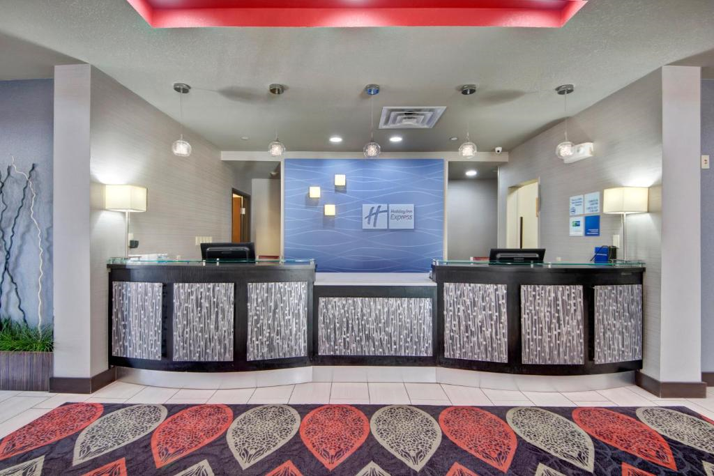 Hotel reception area with two desks, decorative lighting, and a patterned rug. The wall behind features a blue design and a branded sign.