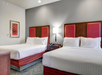 Hotel room with two double beds, red headboards, a nightstand with a lamp, and framed floral wall art.
