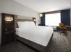 A king bed, bedside lamps, telephone, and desk with chair inside a guest room.