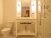 A hotel bathroom with a toilet on the left, a shower with a glass door on the right, and a sink with a mirror and toiletries in the middle.