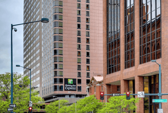 Street view of the Holiday Inn Express Denver Downtown with trees and street lights in front of the large brick building.