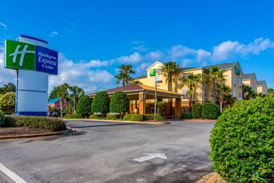Exterior view of a Holiday Inn Express & Suites with clear skies and surrounding greenery.