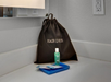 A hair dryer bag, a small green bottle, and two packets placed on a bathroom counter.