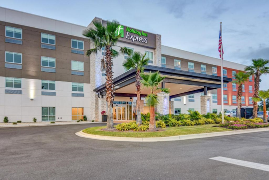 Exterior view of a Holiday Inn Express hotel with palm trees and an American flag.