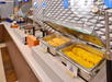 A breakfast buffet with trays containing eggs and pancakes on a counter, with utensils for serving.