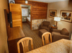 Hotel room with cozy seating area, warm wood accents, and framed art. A bed is visible through an open partition. A TV, desk, and lamp complete the setup.